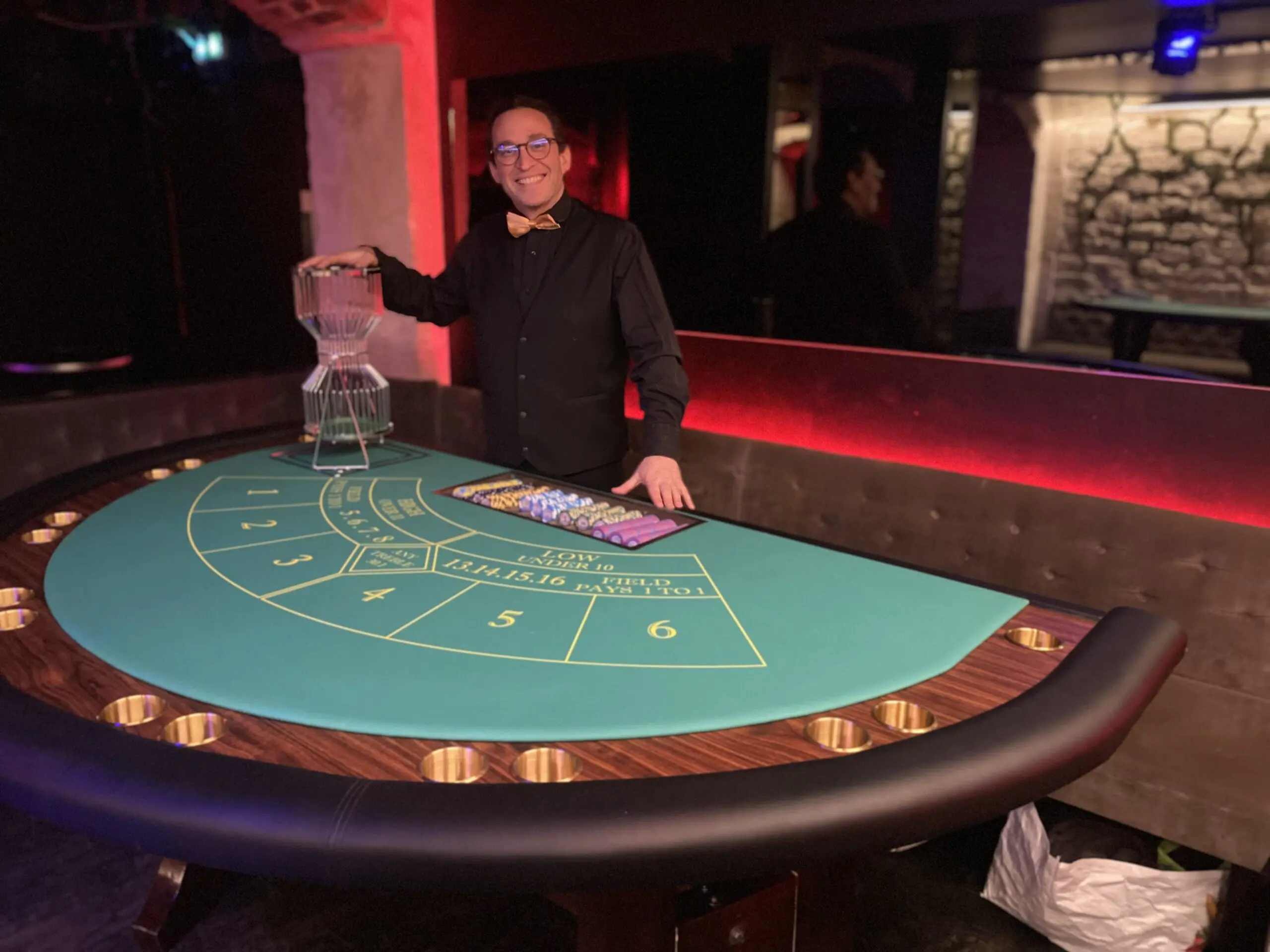 Croupier professionnel souriant animant une table de Sic Bo factice pour une soirée d'entreprise à paris.