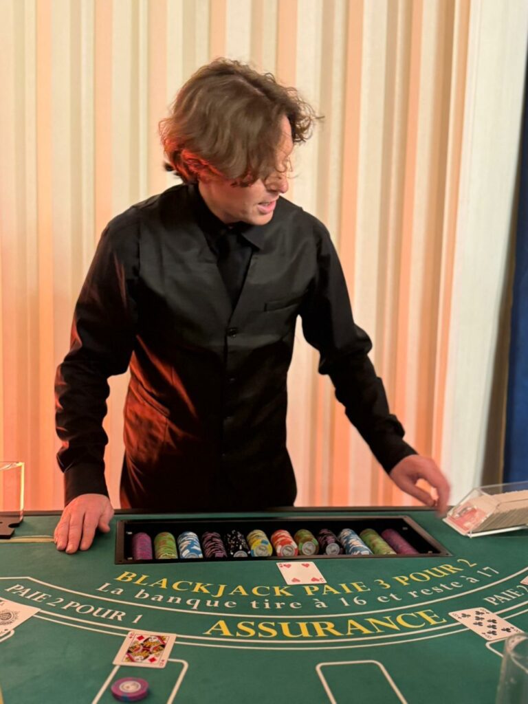 Croupier en chemise noire derrière une table de blackjack, avec un rack de jetons colorés