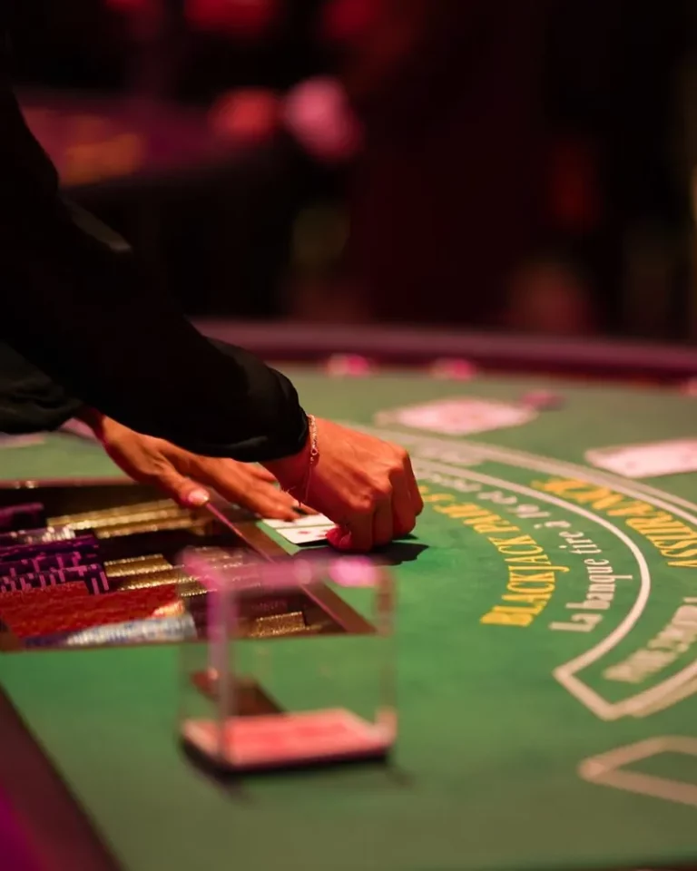 Mains d'une croupière retournant une carte sur un tapis de blackjack lors d'une soirée casino