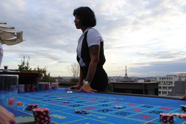 Croupière derrière une table de roulette bleue sur un toit parisien, la tour Eiffel à l'arrière-plan