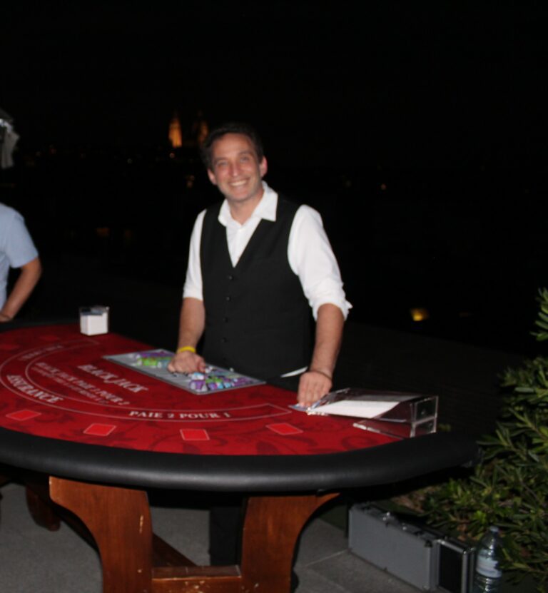 Croupier de blackjack souriant derrière une table rouge, de nuit, lors d'une soirée casino